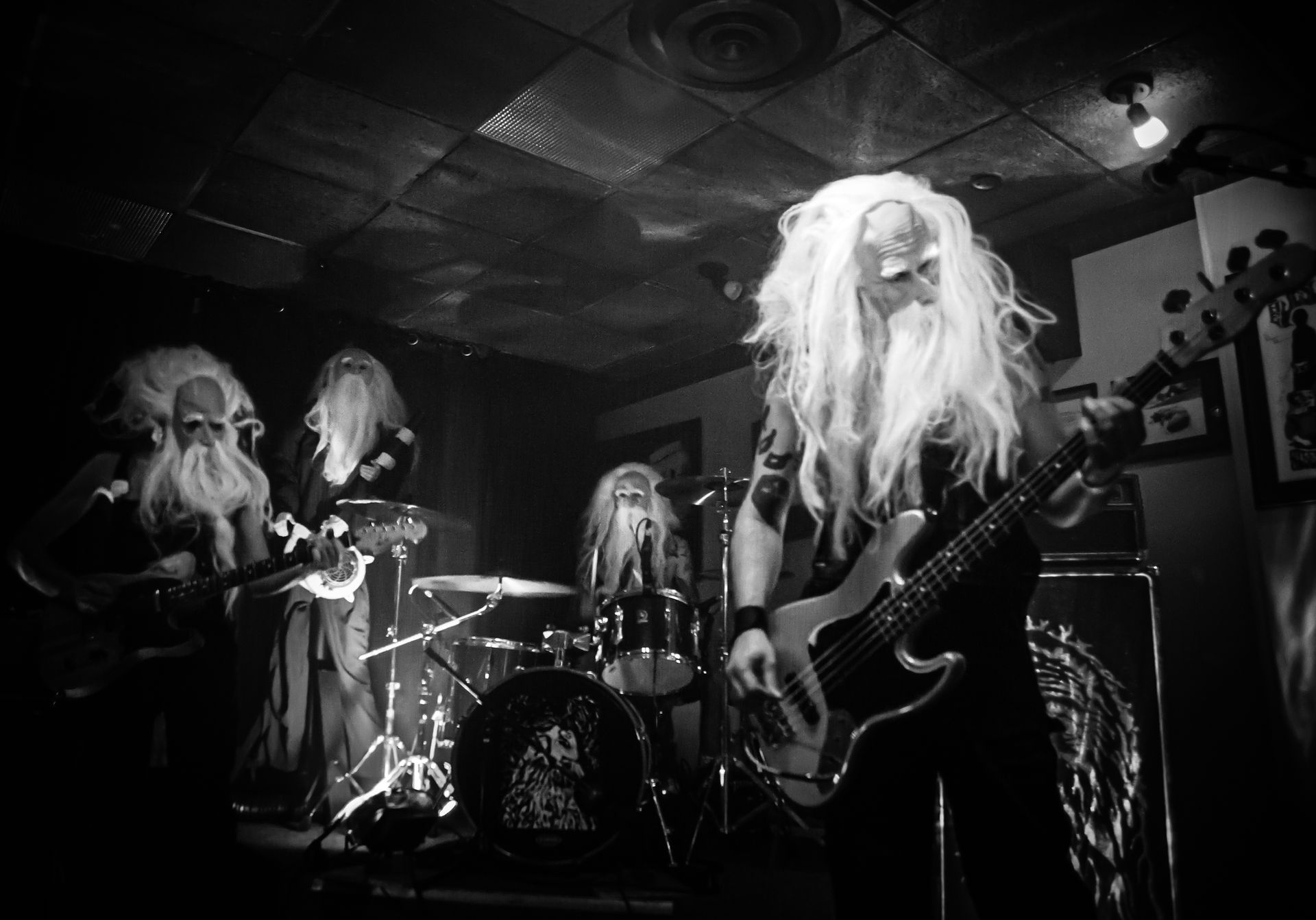Band performing live in dimly lit venue; members wearing long white beards and robes, playing instruments.
