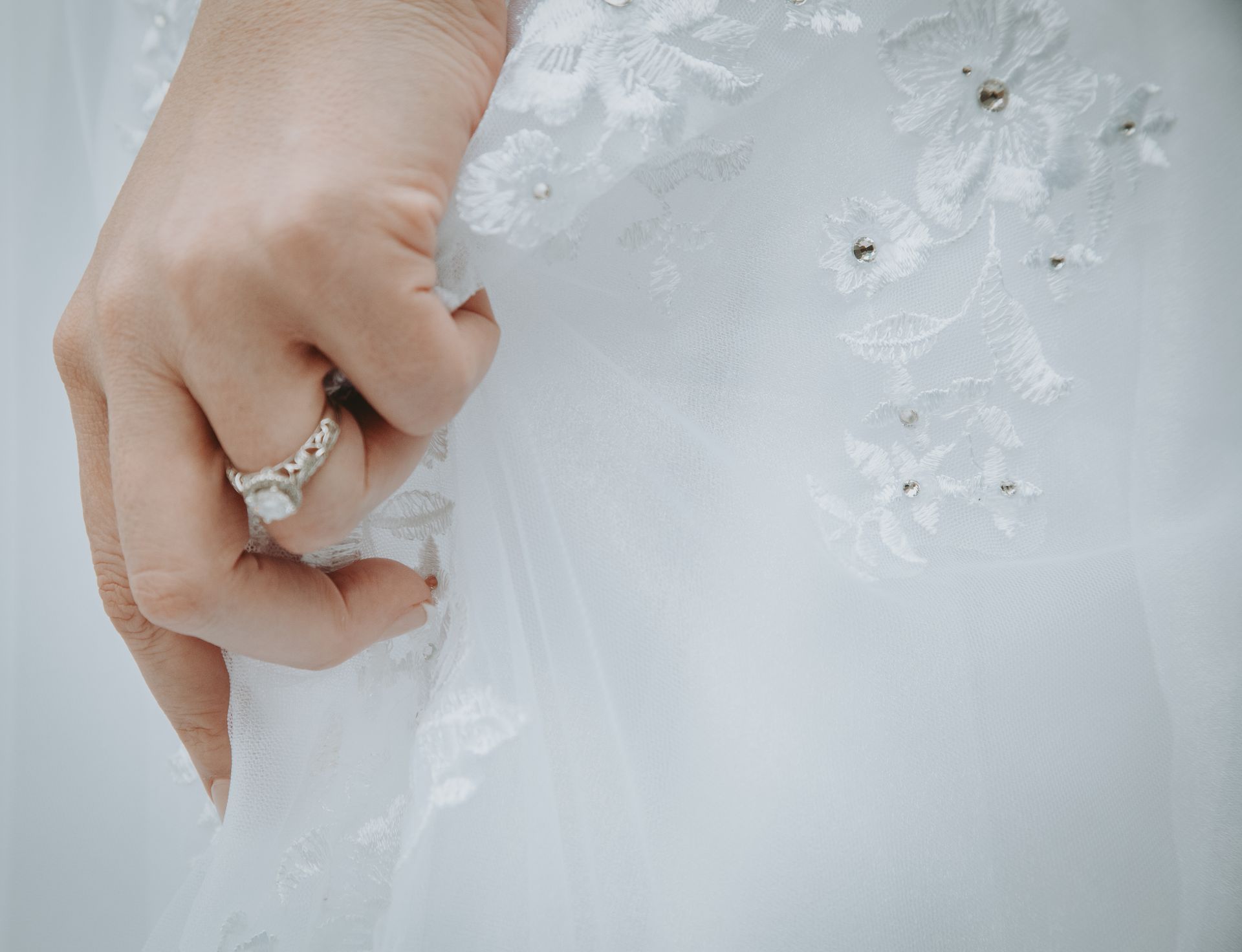 Hand with engagement ring touches white lace wedding dress.