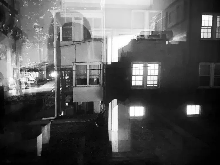 Black and white nighttime shot of buildings, partially transparent, windows glowing.