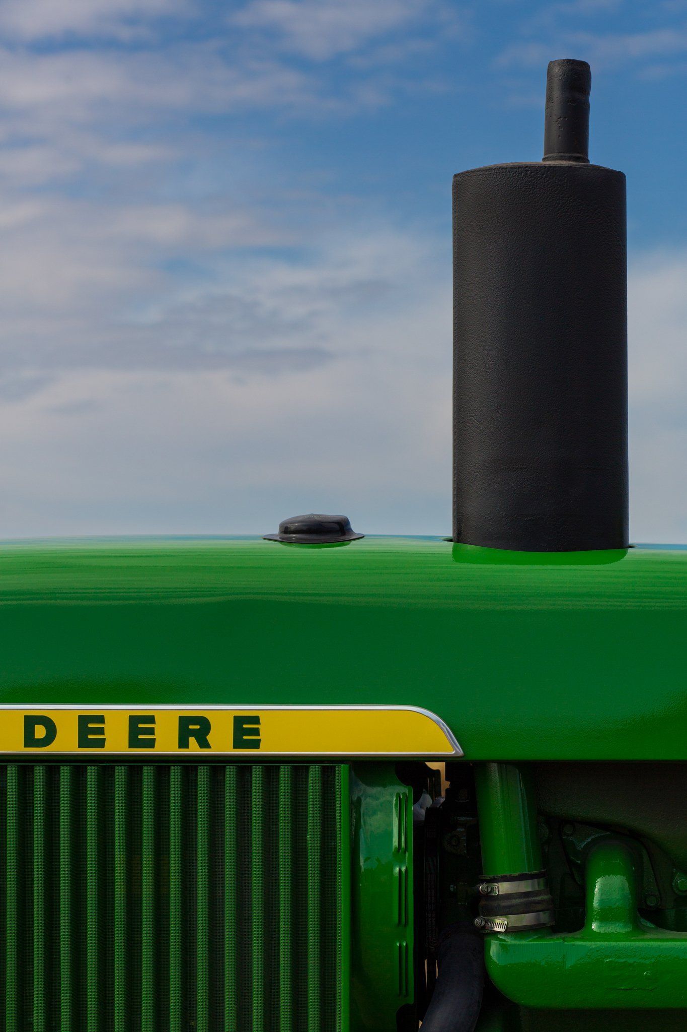 Green John Deere tractor detail with black smokestack against a blue sky.