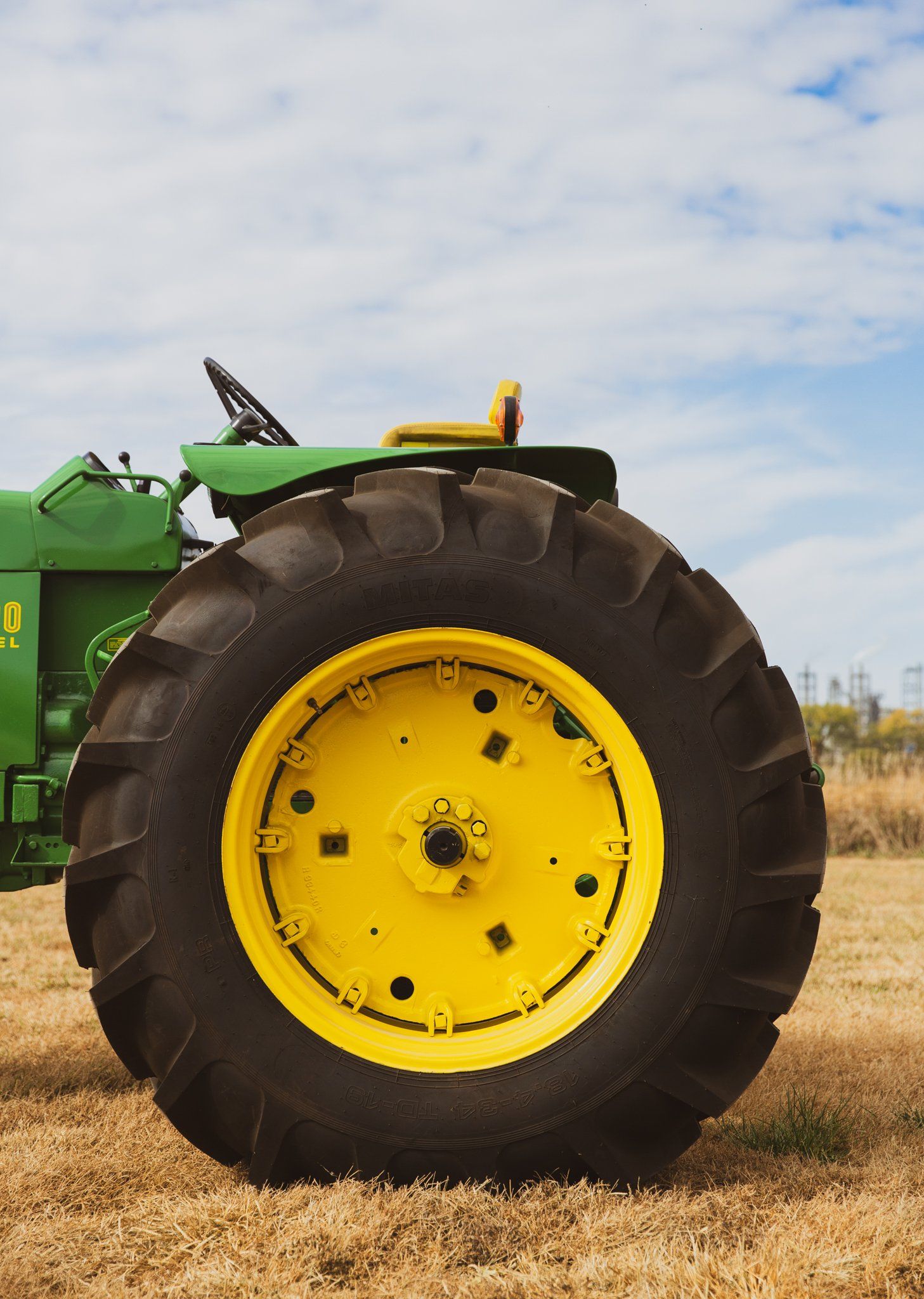 Green and yellow tractor wheel in a field against a cloudy sky.