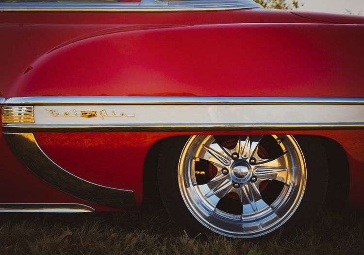 Red classic car with chrome rims and trim, parked on grass.