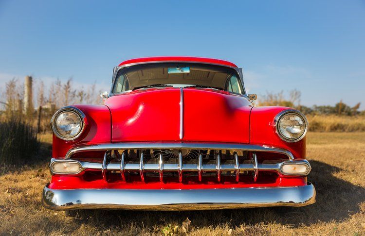 Red classic car parked in a field, bright sunshine and blue sky.