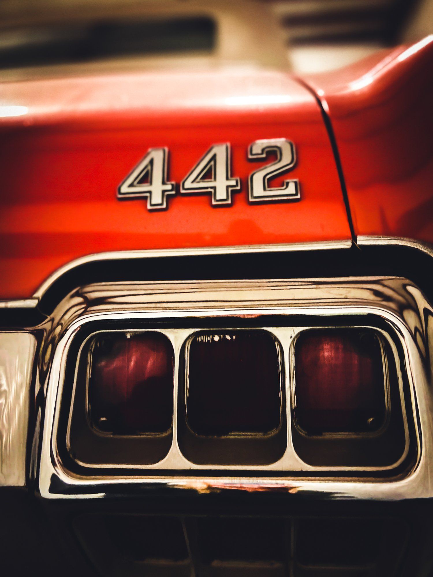 Red 1970 Oldsmobile 442 car's rear, chrome trim and triple taillights.