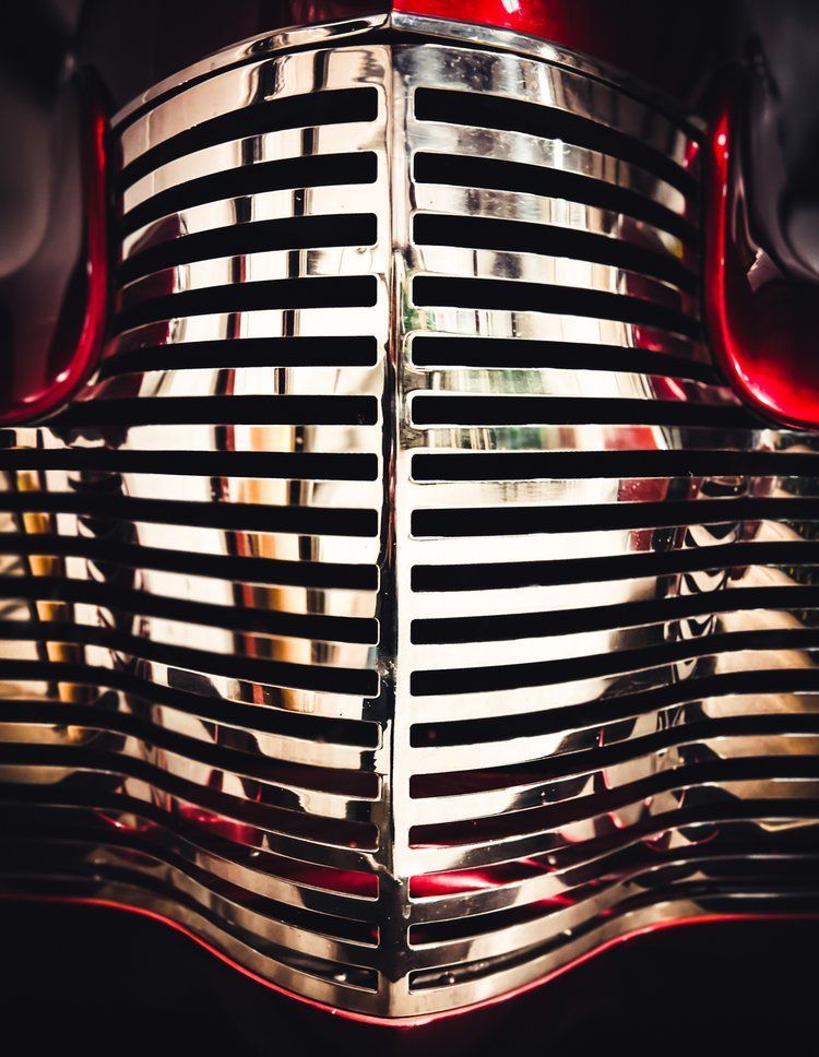 Shiny chrome car grille, red hood, dark setting.