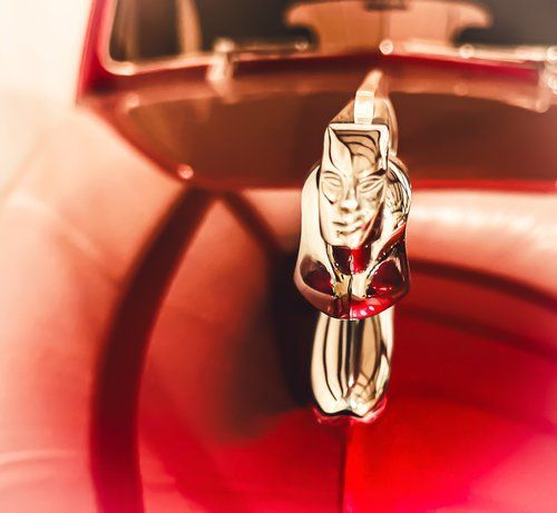 Close-up of a chrome hood ornament on a red classic car.