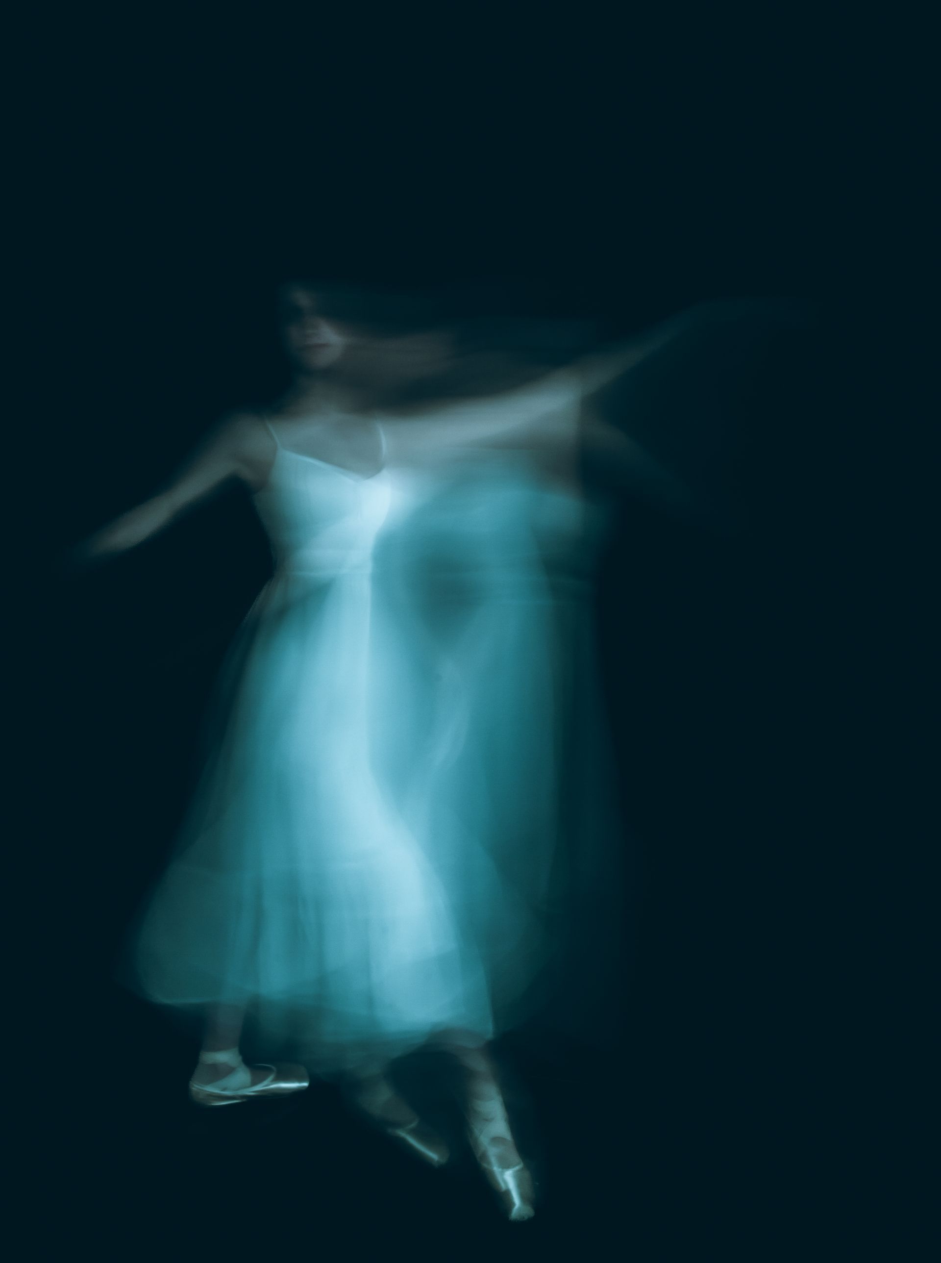 Blurred image of a ballerina in a white dress, arms outstretched, dancing against a dark background.