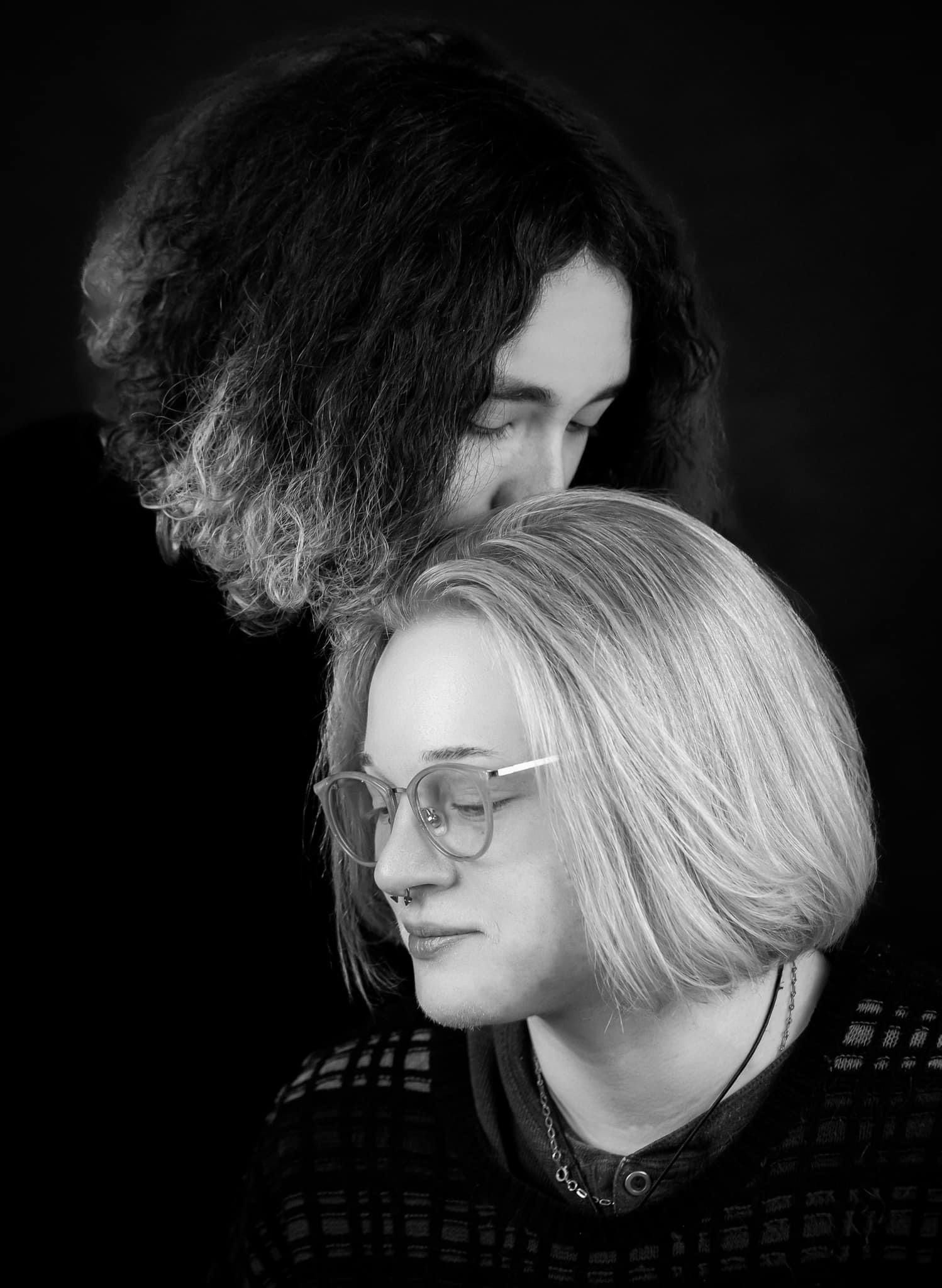 Two people in black and white portrait. One person's hair is over the other's head and both are looking down.