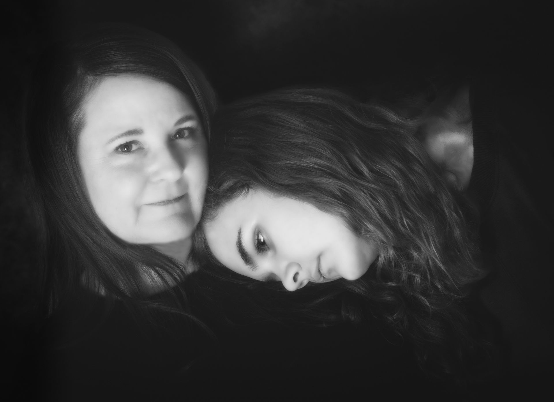 Two women, one smiling, the other resting head on her shoulder, both in black and white.