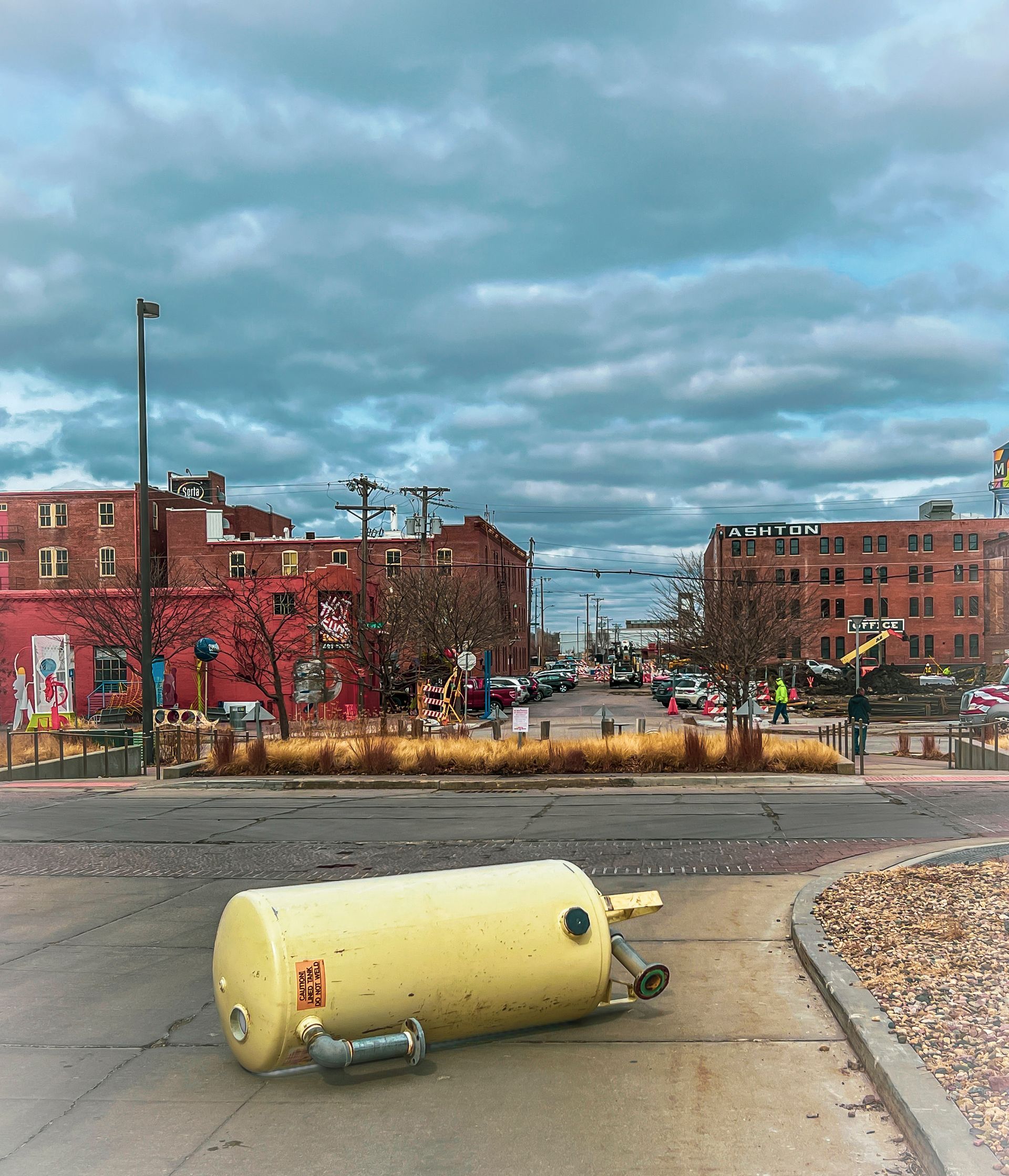 A yellow water heater on a sidewalk in a city street, overcast sky, red brick buildings.