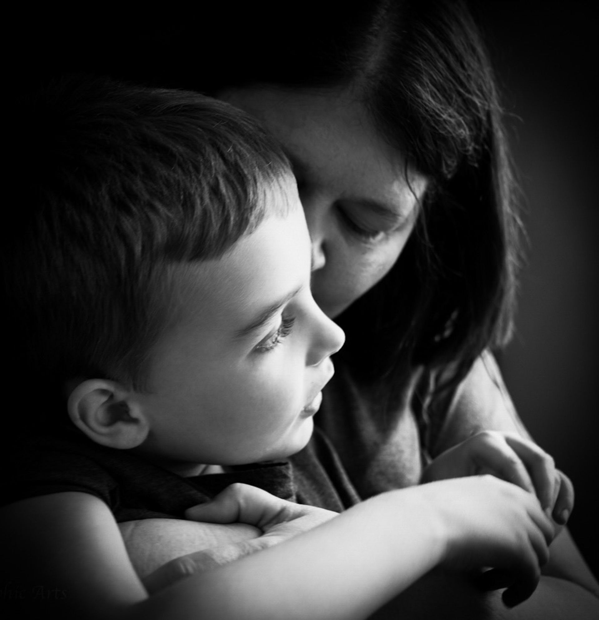Mother embracing a young child, cheek to cheek, in black and white.