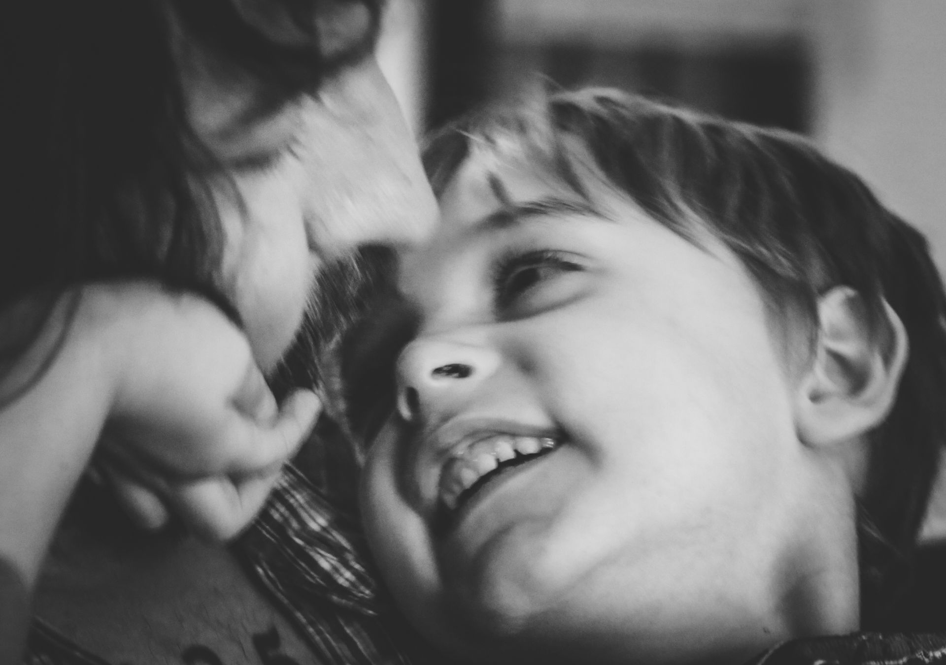 Two children, one smiling, touching noses, in black and white.
