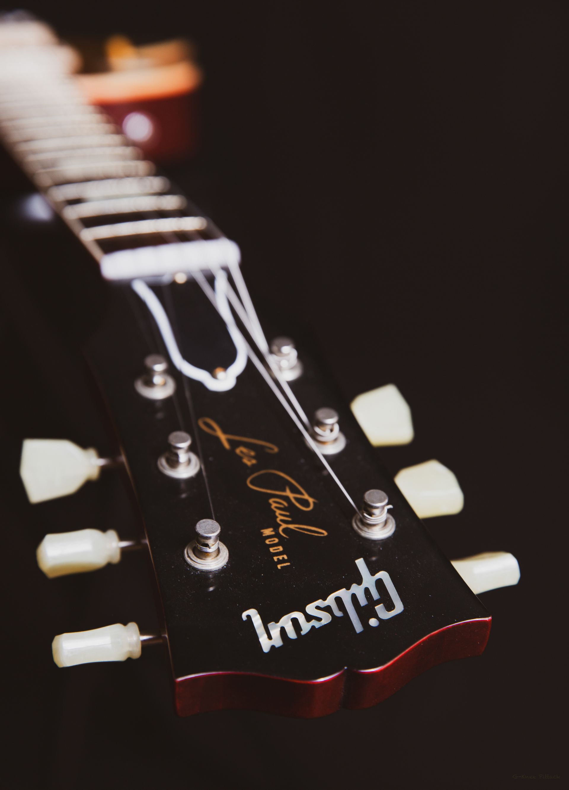 Close-up of a Gibson Les Paul guitar headstock, black with white tuning pegs and strings, and the 