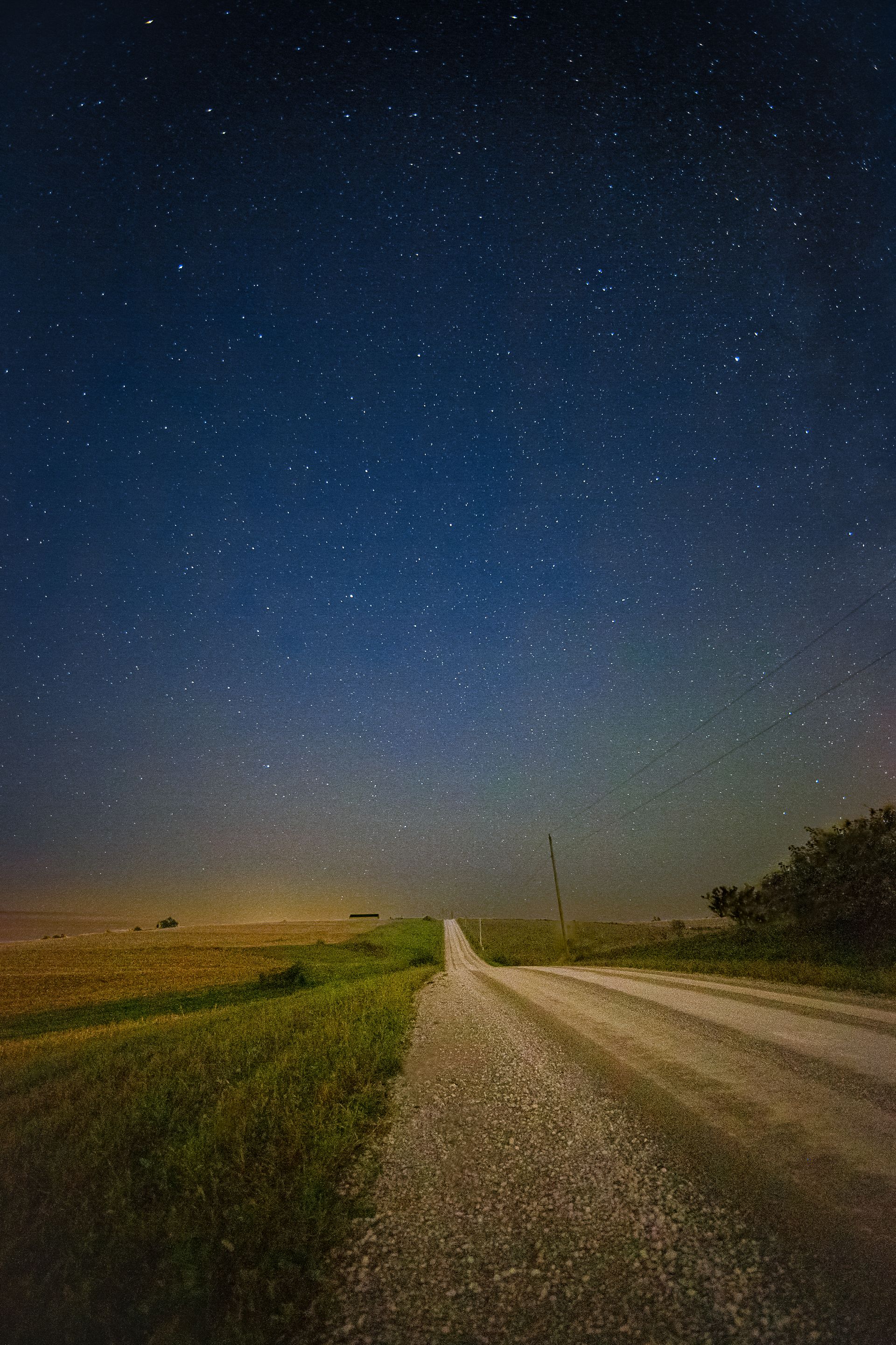 Gravel road leading towards the starry night sky over a grassy field.
