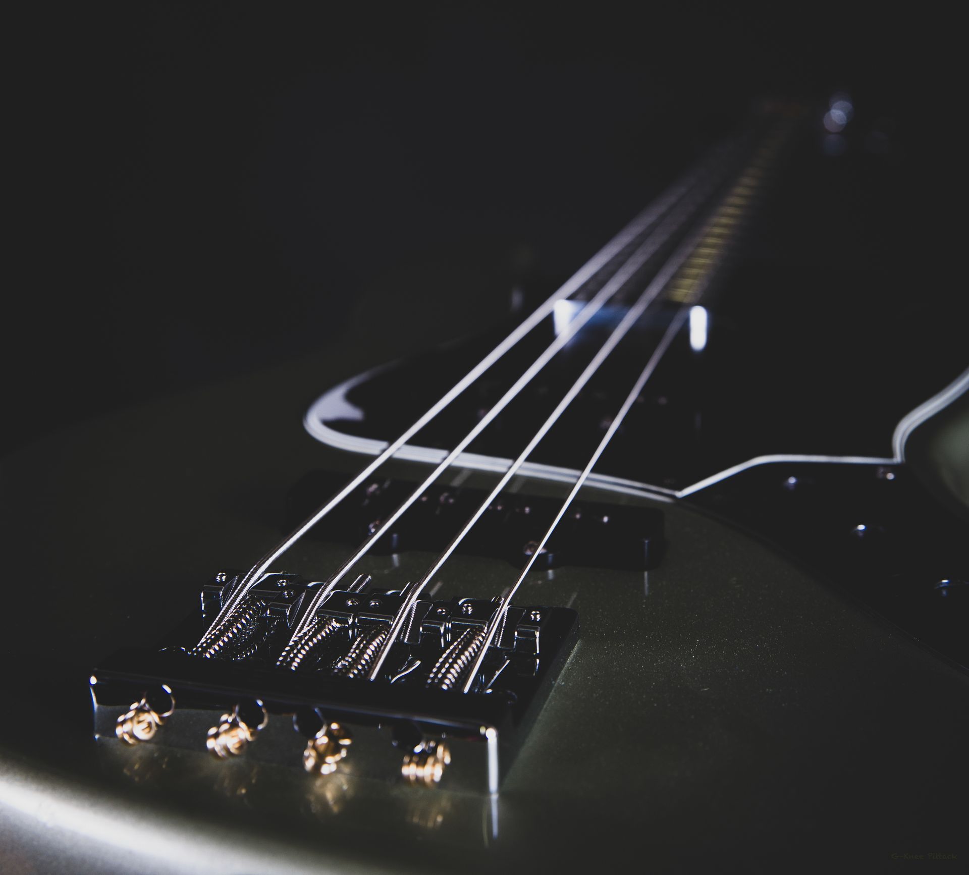 Close-up of an olive green bass guitar with strings, against a dark background.