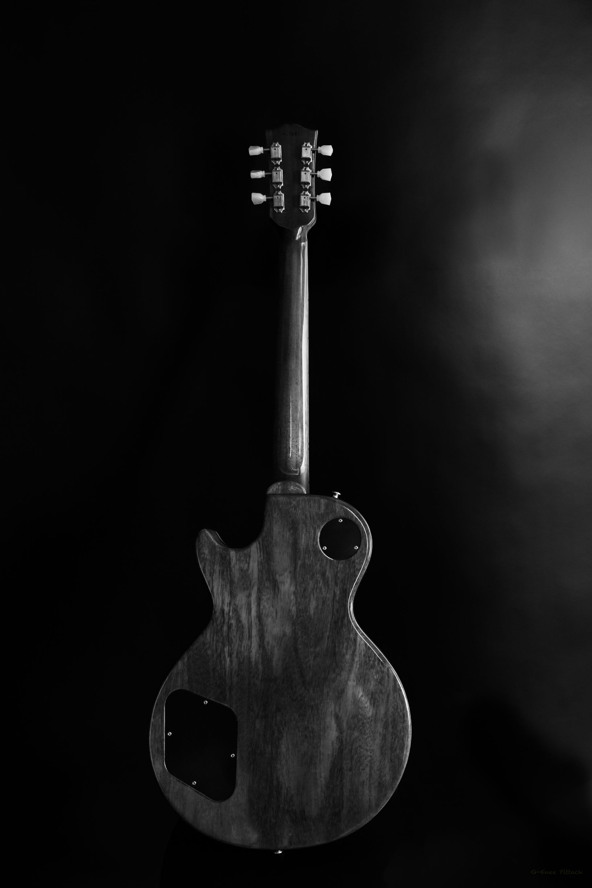 Black and white guitar. Back view, dark wood finish against black background.