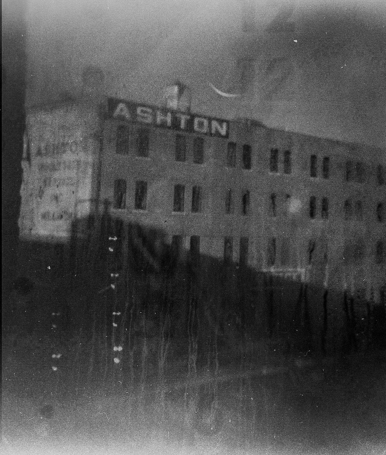 Old, grainy black and white photo of the Ashton building. Large sign on top.