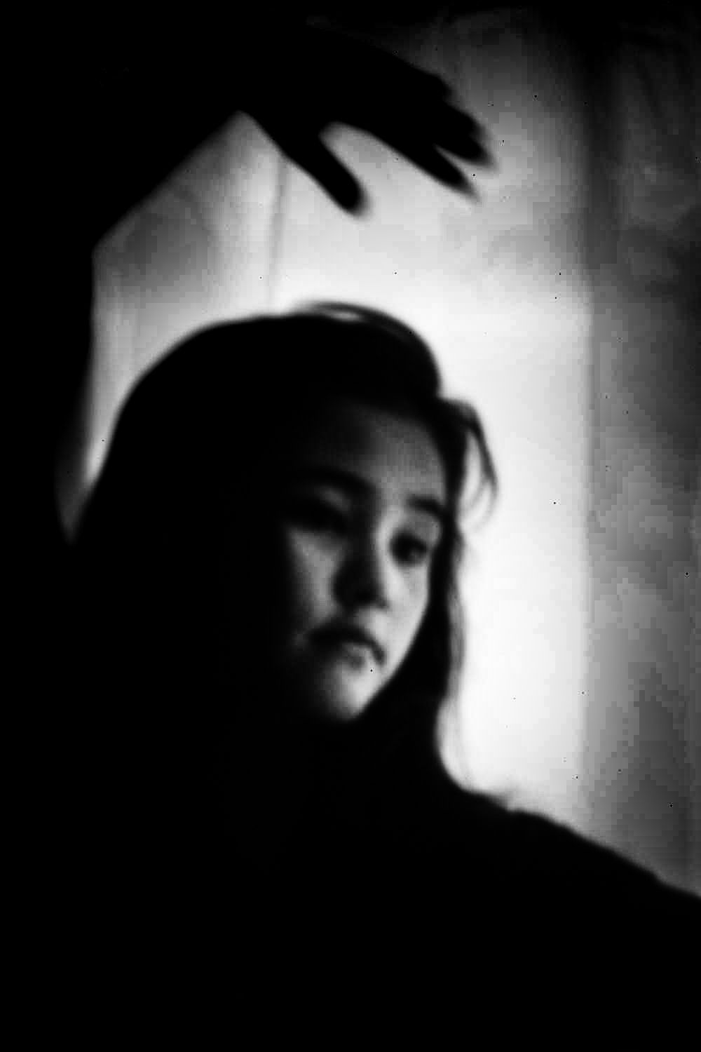 Black and white portrait of a woman reaching upward. Her face is slightly blurred, looking pensive.