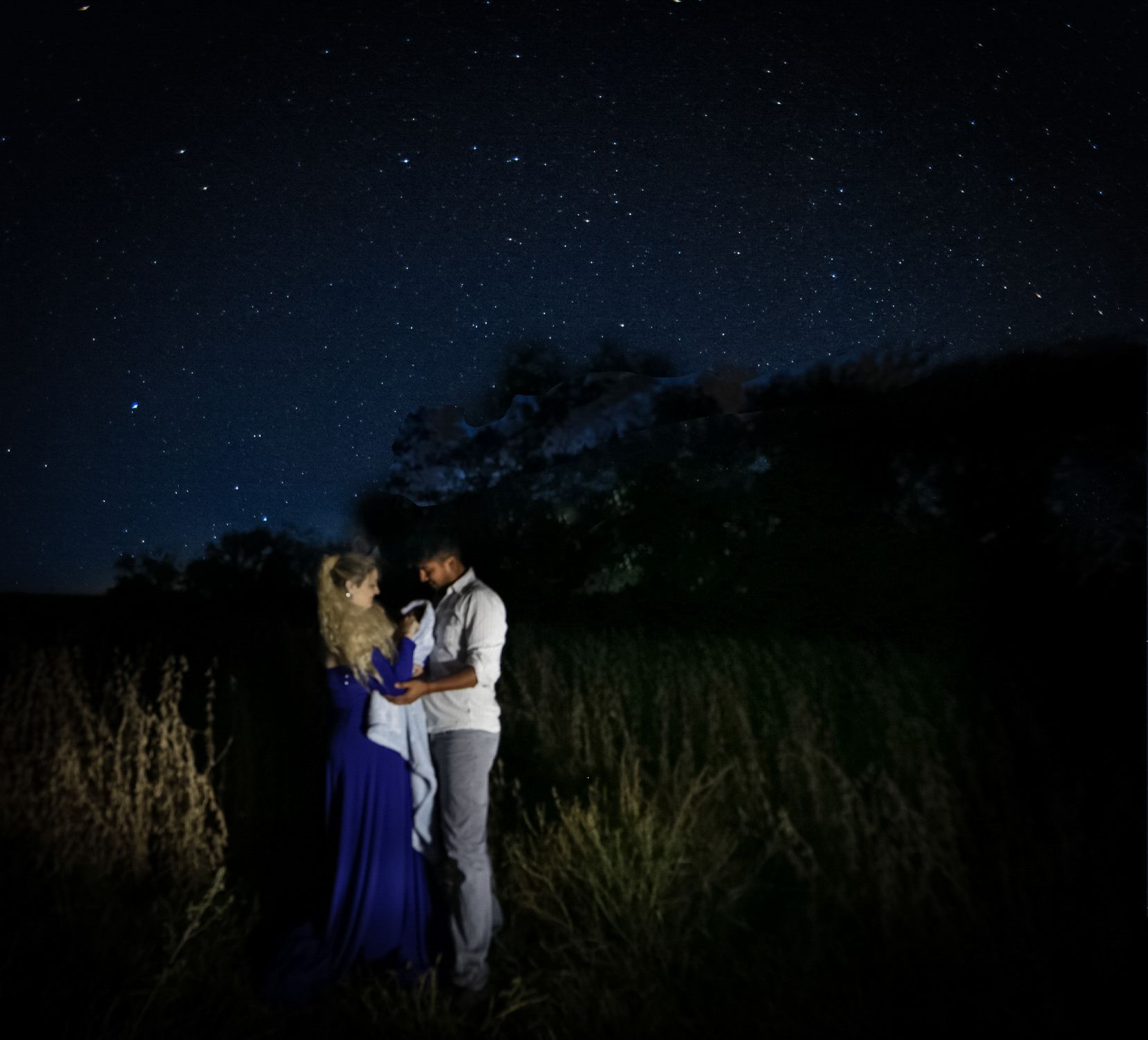 Couple embracing under a starry night sky, standing in a field of tall grass.