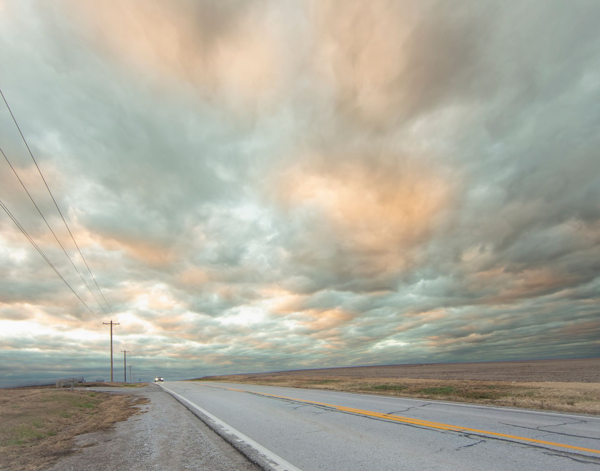 Road stretching to horizon beneath a dramatic, cloudy sky with warm colors.