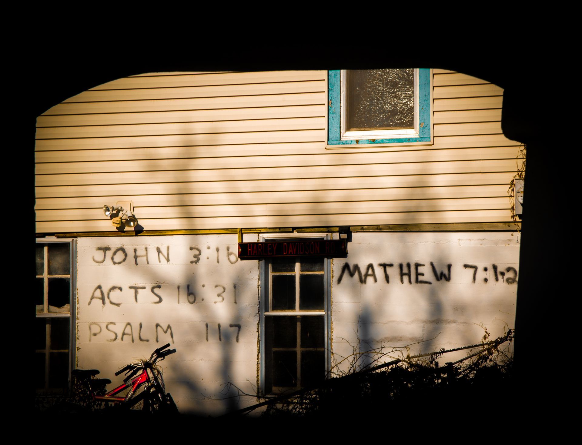 A weathered building with Bible verses painted on its side. A bicycle sits in front.