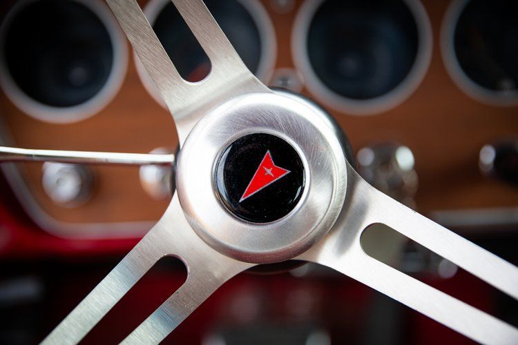 Silver steering wheel with Pontiac logo, brown dashboard in background.