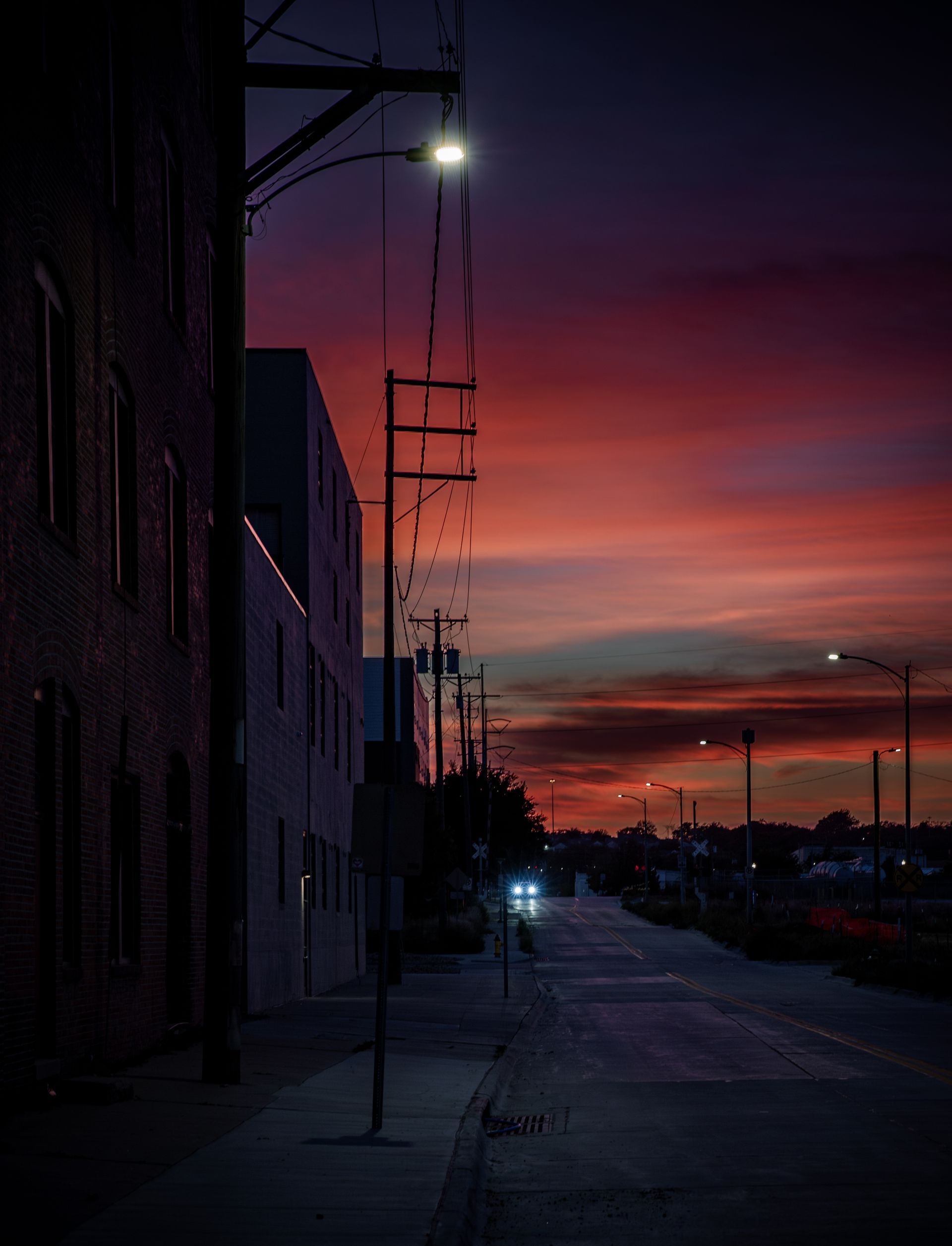 Night street scene under a colorful sunset; brick building and power lines on the left, street and buildings on the right.