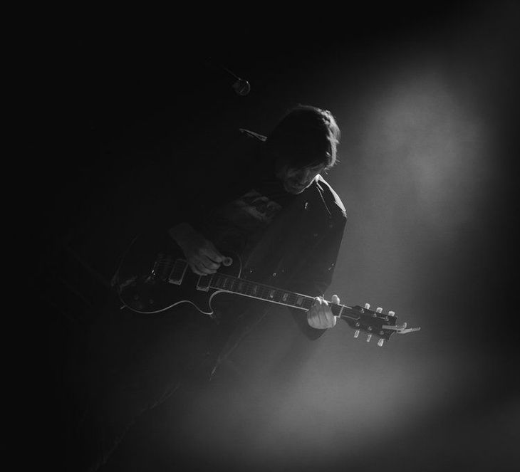 Guitarist in dark setting, illuminated by spotlight, playing an electric guitar.