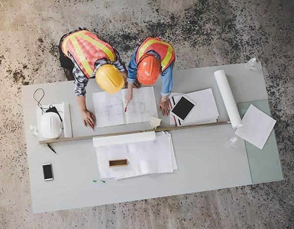 Two Construction Workers Are Looking At A Blueprint On A Table — Chris Stolk Constructions In Kanahooka, NSW