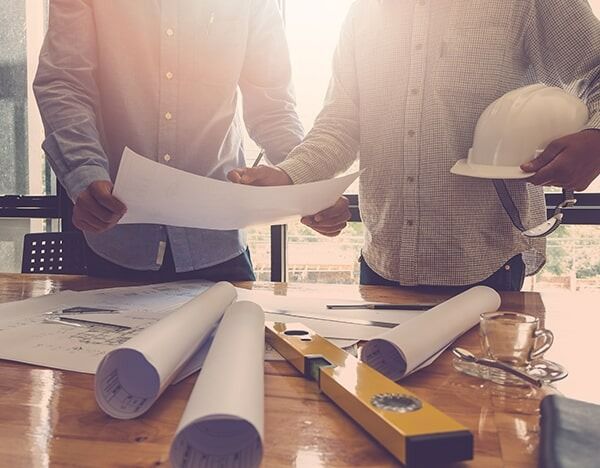 Two Men Are Sitting At A Table Looking At A Blueprint — Chris Stolk Constructions In Kanahooka, NSW