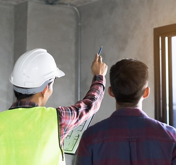 A Man Wearing A Hard Hat And Safety Vest Is Standing Next To Another Man — Chris Stolk Constructions In Kanahooka, NSW