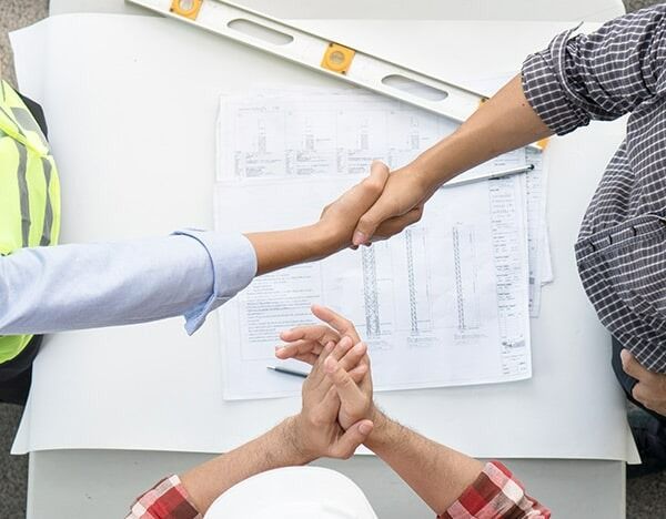 A Group Of People Shaking Hands Over A Table — Chris Stolk Constructions In Kanahooka, NSW