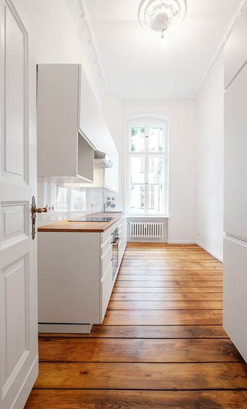 A Long Hallway Leading To A Kitchen With Wooden Floors And White Cabinets — Chris Stolk Constructions In Albion Park, NSW