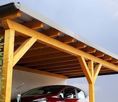 A Red Car Is Parked Under A Wooden Carport — Chris Stolk Constructions In Wollongong, NSW