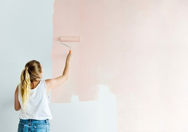 A Woman Is Painting A Wall With A Paint Roller — Chris Stolk Constructions In Kanahooka, NSW