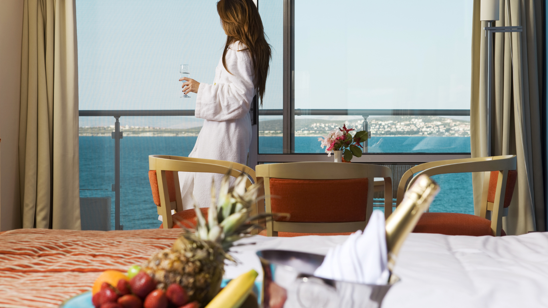 A woman is standing on a balcony holding a glass of wine.