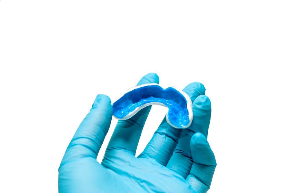 A Person Wearing Blue Gloves Is Holding a Blue Mouthguard — Bromley's Denture Clinic in Tweed Heads South, NSW