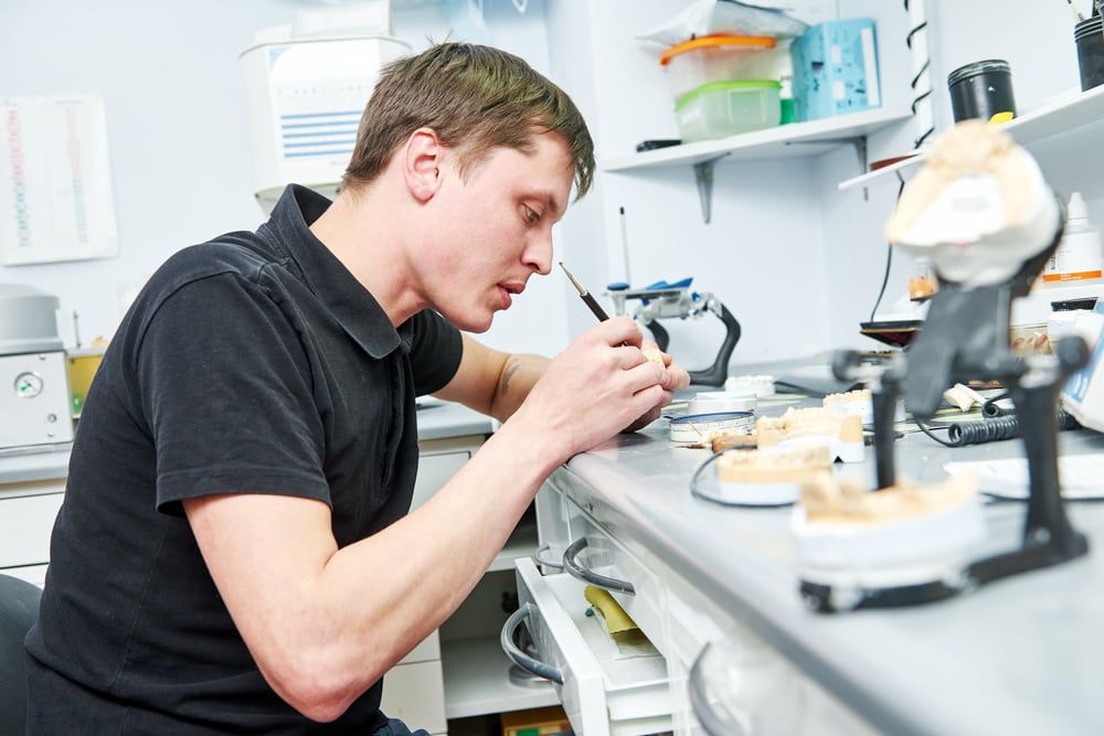 A Man Is Working on A Dental Model in A Lab — Bromley's Denture Clinic in Tweed Heads South, NSW