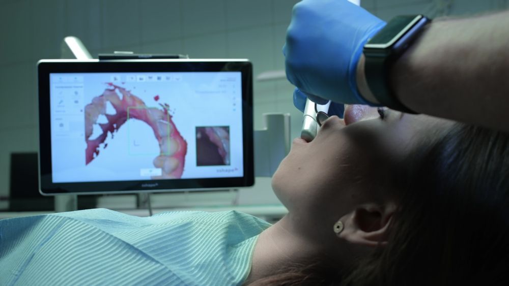 A Woman in a Dental Chair and Doctor With Gloved Hands Uses a Device — Bromley's Denture Clinic in Tweed Heads South, NSW