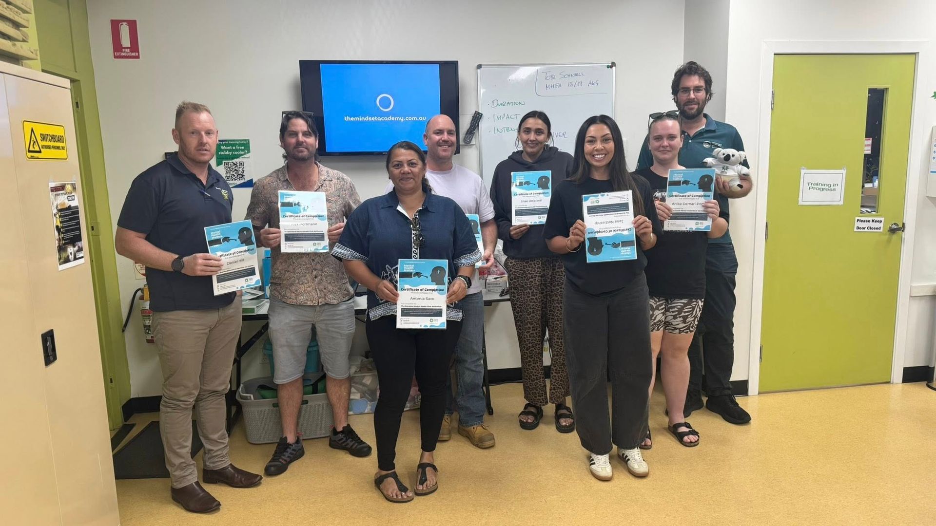 Group of people holding certificates, smiling in a room with a whiteboard and screen. Group of people holding certificates, smiling in a room with a whiteboard and screen.