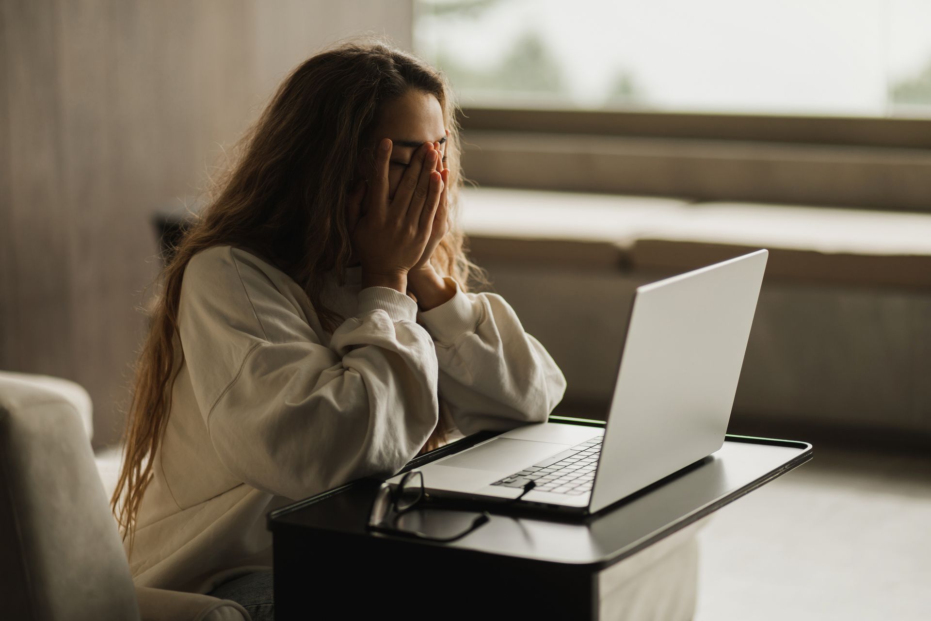 Person sitting at a laptop, covering their face with hands, looking stressed.
