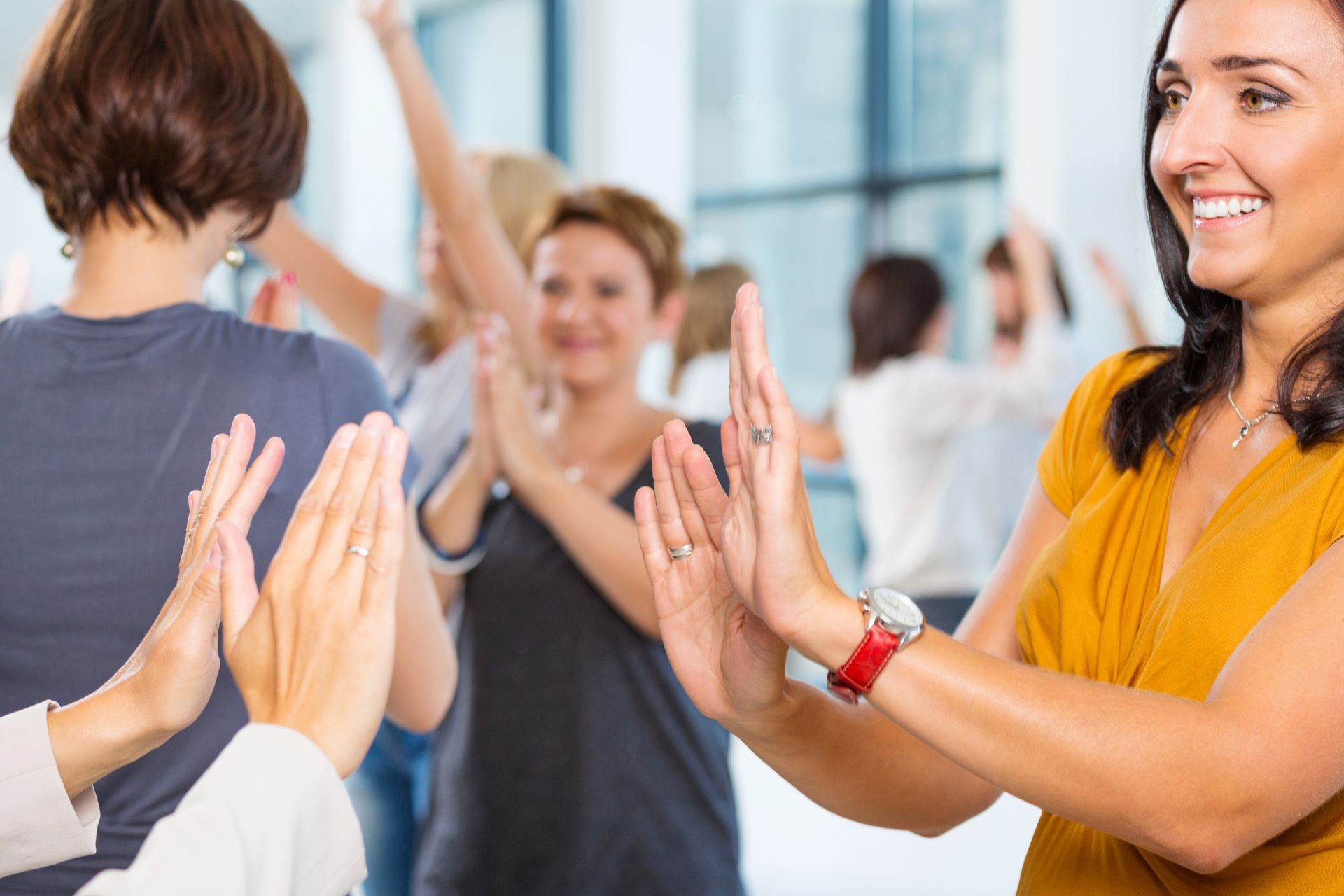 People clapping in a bright office setting. Woman in yellow top smiles, others in background. People clapping in a bright office setting. Woman in yellow top smiles, others in background.