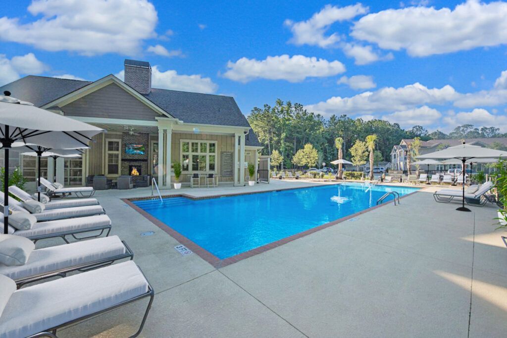 A large swimming pool surrounded by chairs and umbrellas in front of a house.