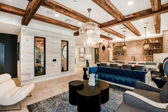 Lounge room with wood beams, blue velvet couch, and brick wall kitchen.