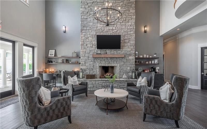 Living room with stone fireplace, gray armchairs around a coffee table, and a large chandelier.