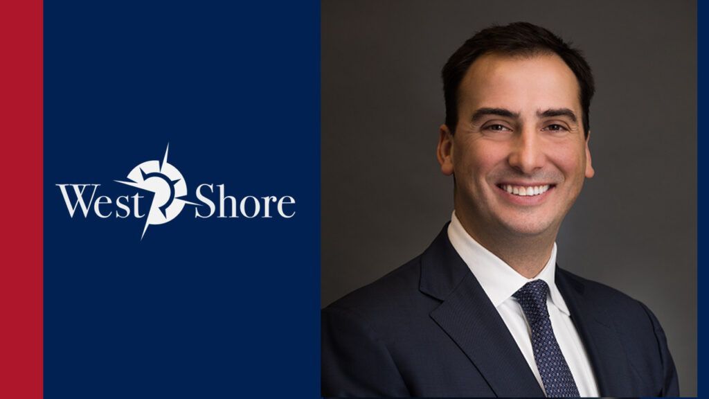A man in a suit and tie is smiling in front of a west shore logo.