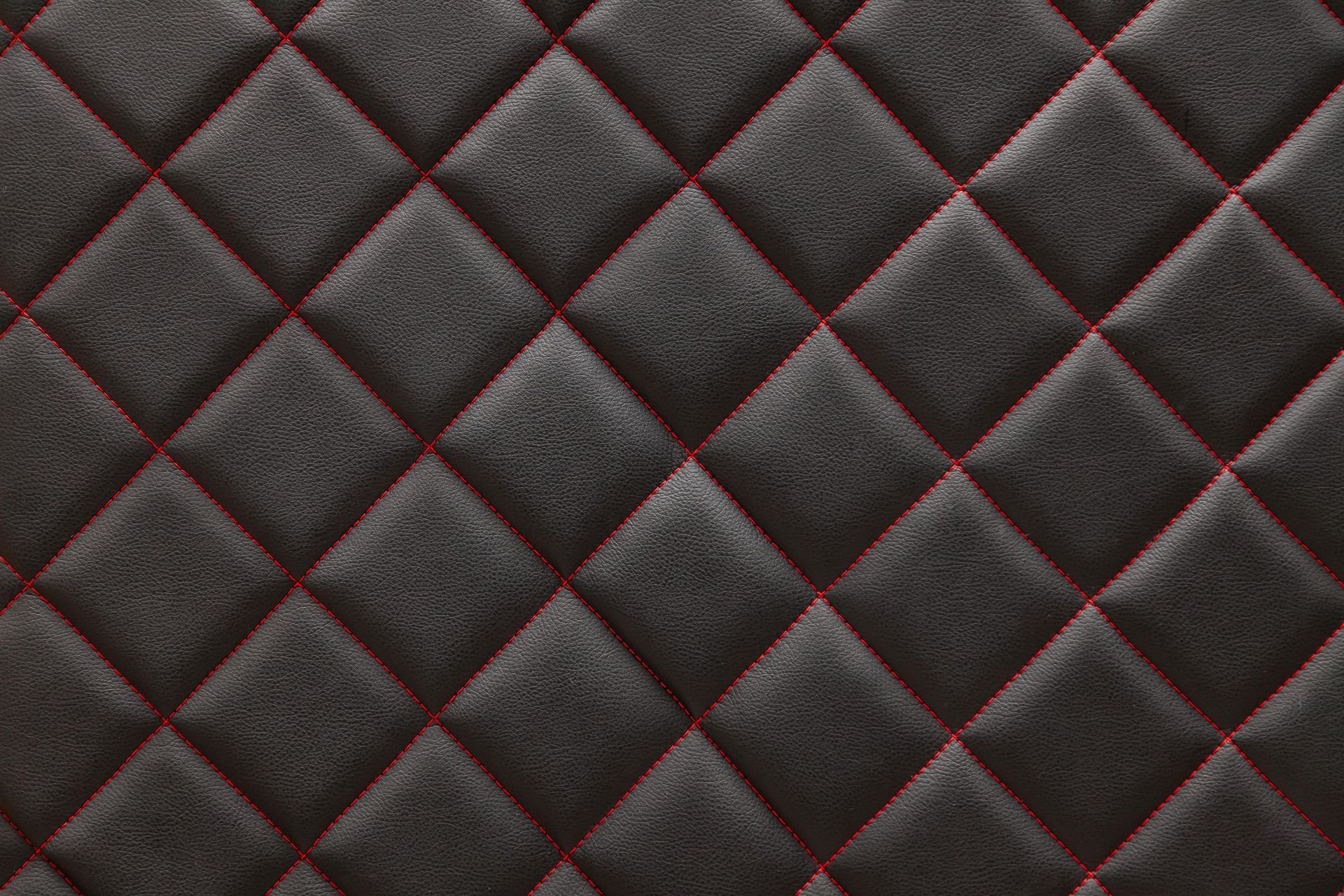 a close up of a black quilted leather texture with red stitching .