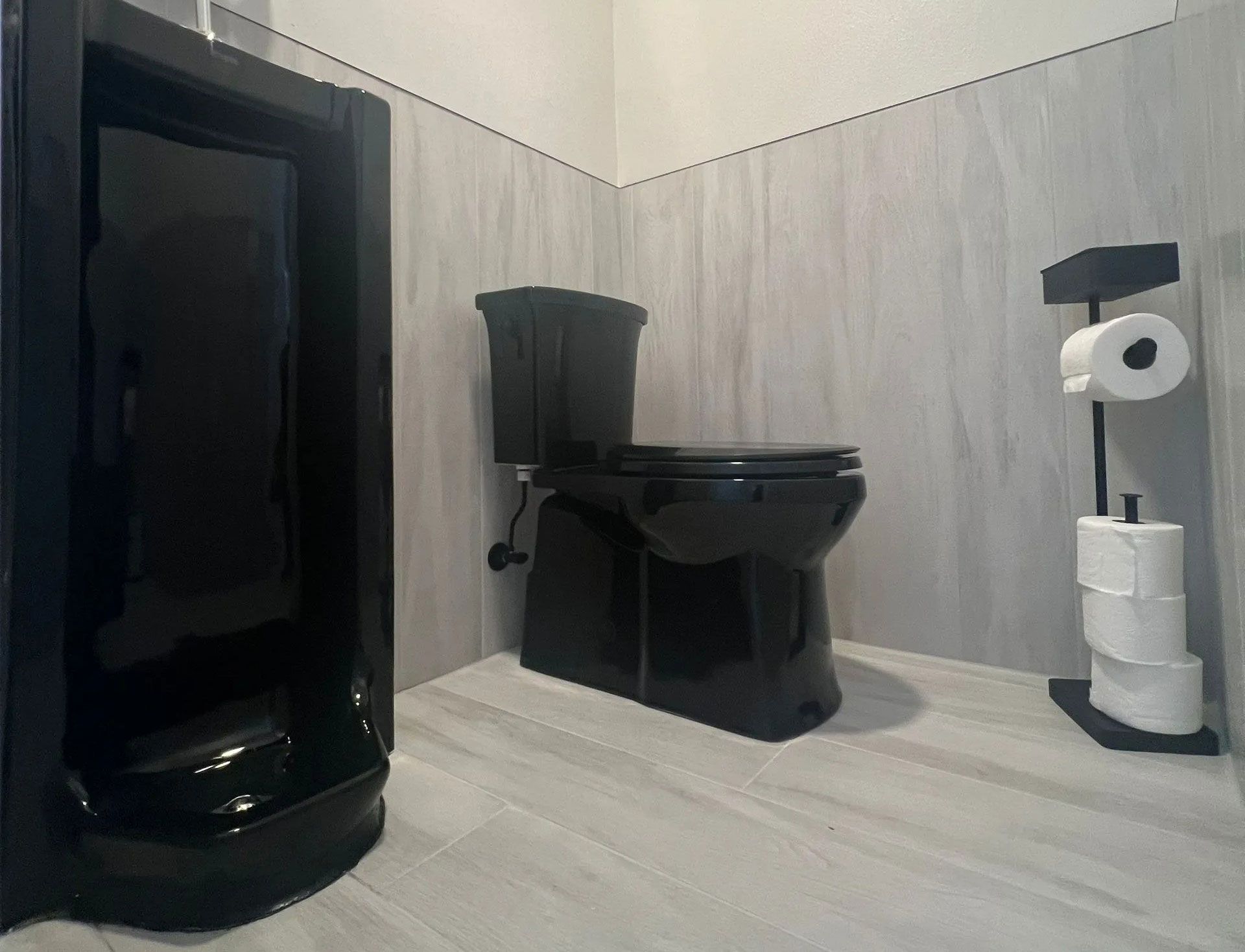 There is a large island in the middle of the kitchen. A black toilet is in a bathroom next to a stack of toilet paper.