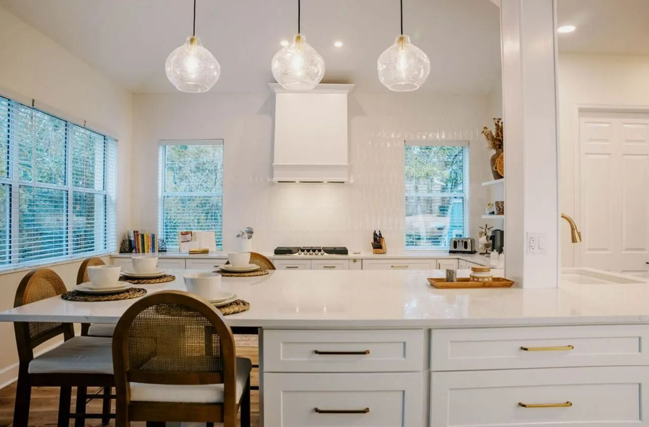 A kitchen with white cabinets , a large island , a table and chairs.