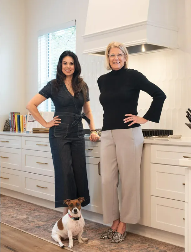 Two women are standing next to each other in a kitchen with a dog.